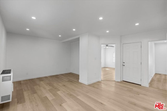 unfurnished room with heating unit, ceiling fan, radiator heating unit, and light hardwood / wood-style flooring