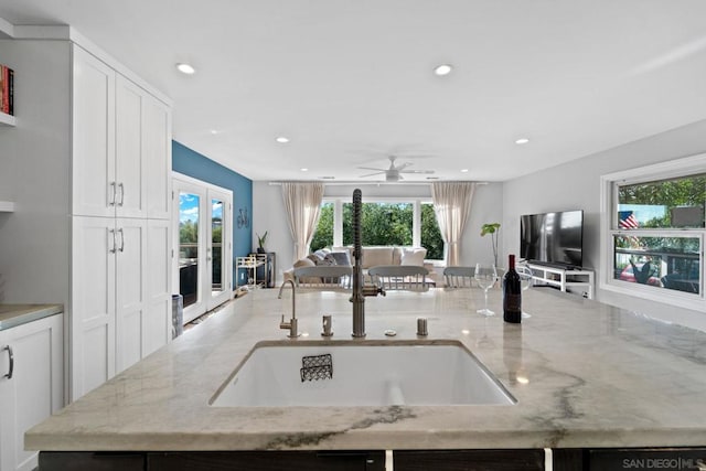 kitchen featuring white cabinets, light stone countertops, sink, and ceiling fan