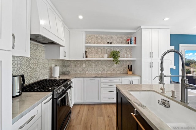 kitchen with white cabinets, sink, stainless steel gas range, light hardwood / wood-style floors, and custom range hood