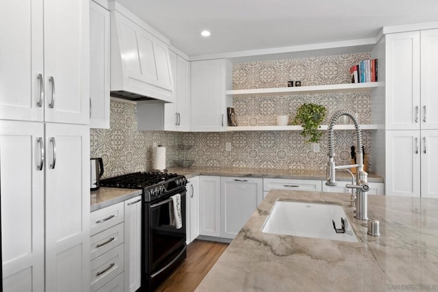 kitchen featuring high end range, light stone counters, custom exhaust hood, sink, and white cabinetry