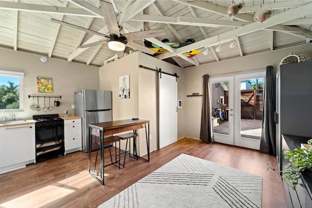 kitchen with stainless steel refrigerator, a barn door, black range with gas cooktop, and vaulted ceiling with beams