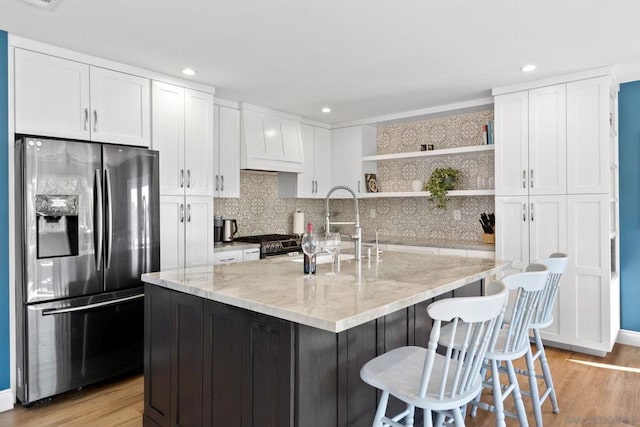 kitchen featuring light stone counters, light wood-type flooring, an island with sink, and appliances with stainless steel finishes