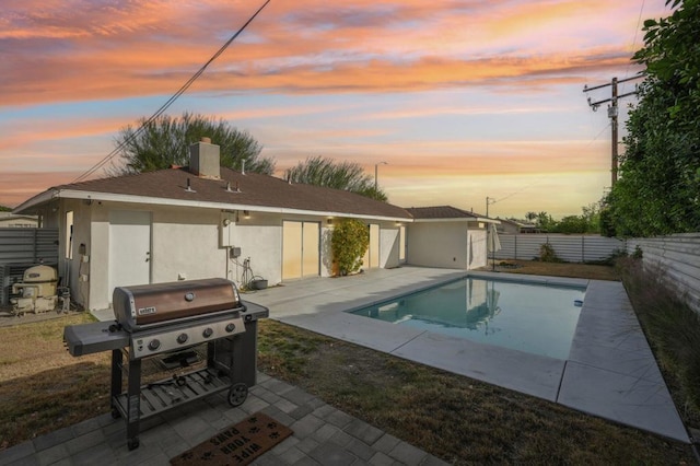 pool at dusk featuring a grill, an outbuilding, and a patio