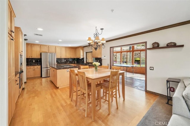 dining area with an inviting chandelier, sink, crown molding, and light hardwood / wood-style floors