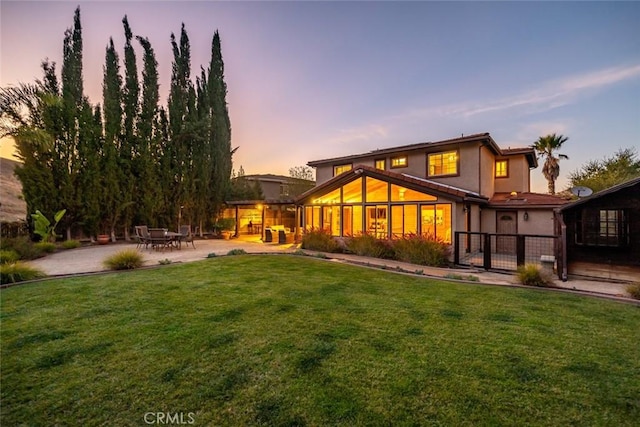 back house at dusk featuring a lawn and a patio area