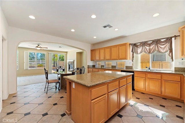 kitchen featuring light stone counters, ceiling fan, sink, dishwasher, and a kitchen island