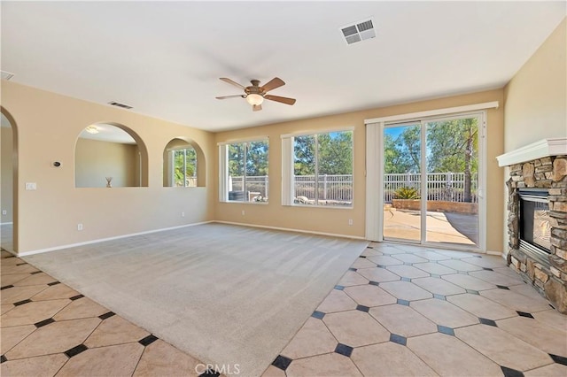 unfurnished living room featuring light carpet, a stone fireplace, a wealth of natural light, and ceiling fan