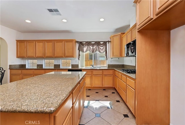 kitchen featuring light stone countertops, sink, a center island, stainless steel gas stovetop, and light tile patterned flooring