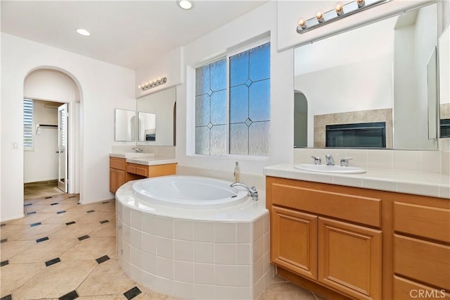 bathroom featuring tile patterned floors, vanity, tiled bath, and a tiled fireplace