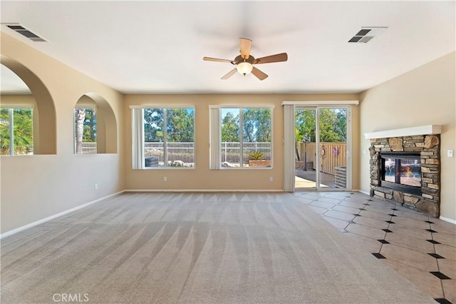 unfurnished living room featuring ceiling fan, a stone fireplace, and light colored carpet