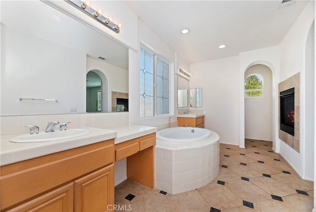 bathroom featuring tile patterned floors, vanity, a tile fireplace, and tiled bath