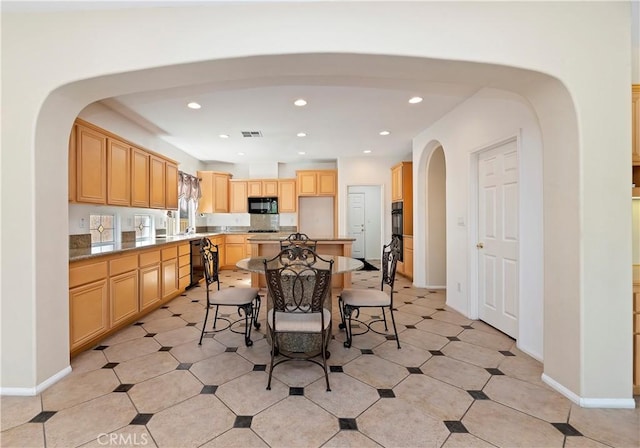 kitchen with light brown cabinetry, a kitchen island, a kitchen breakfast bar, and black appliances