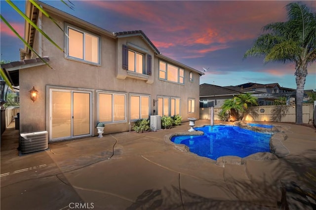 pool at dusk with cooling unit, an in ground hot tub, and a patio