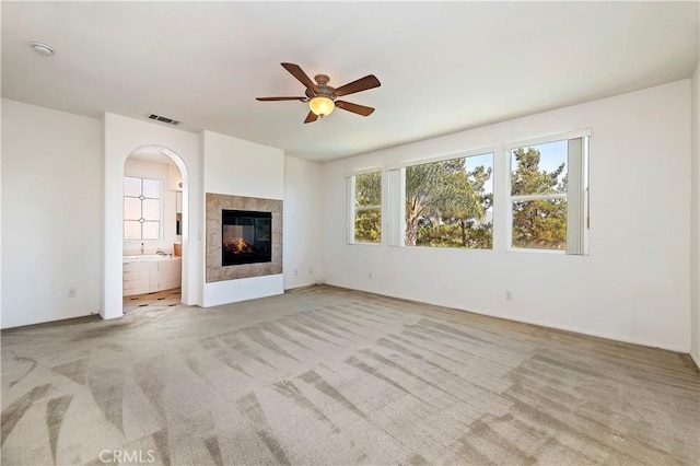 unfurnished living room featuring ceiling fan, a fireplace, and light colored carpet