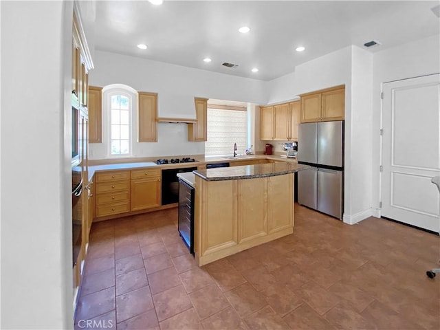 kitchen with light brown cabinets, white gas stovetop, a sink, a kitchen island, and freestanding refrigerator