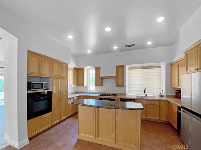 kitchen featuring visible vents, dark stone countertops, a center island, black appliances, and a sink