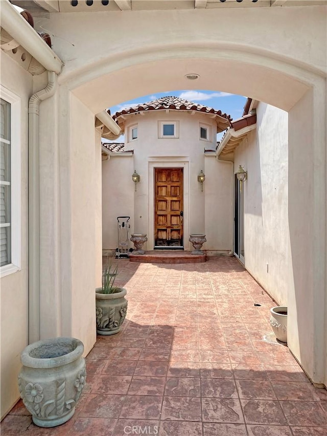 entrance to property with a patio, a tiled roof, and stucco siding