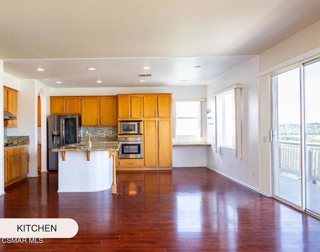 kitchen with light stone countertops, stainless steel appliances, dark hardwood / wood-style floors, a kitchen bar, and a kitchen island