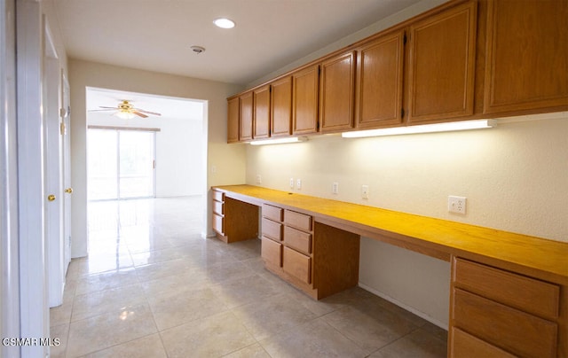 unfurnished office with light tile patterned floors, built in desk, and ceiling fan