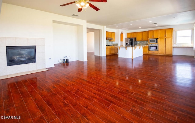 unfurnished living room featuring dark hardwood / wood-style floors, ceiling fan, and a tiled fireplace