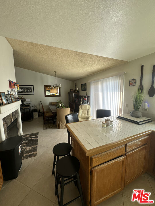 kitchen with pendant lighting, a tile fireplace, vaulted ceiling, light tile patterned flooring, and tile countertops