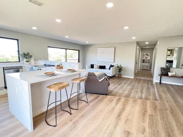 kitchen featuring range, a kitchen breakfast bar, dishwasher, light hardwood / wood-style floors, and white cabinets