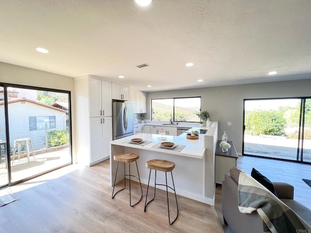 kitchen with sink, light hardwood / wood-style flooring, a breakfast bar, stainless steel appliances, and white cabinets