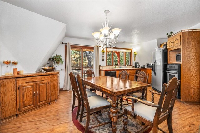 dining area featuring a textured ceiling, light wood-type flooring, lofted ceiling, and a notable chandelier