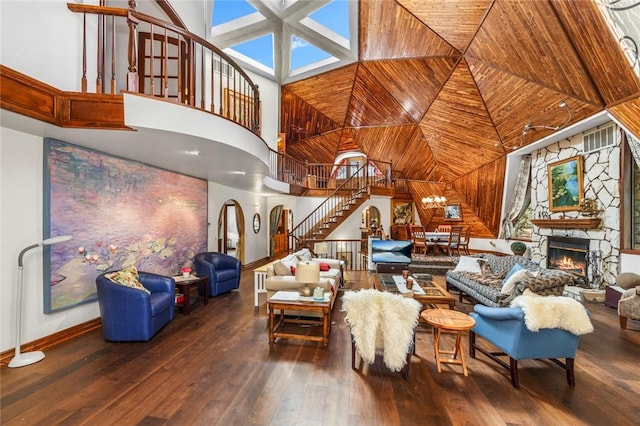 living room featuring hardwood / wood-style floors, a stone fireplace, a towering ceiling, and an inviting chandelier