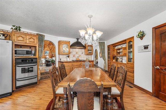 dining space with light hardwood / wood-style floors, a textured ceiling, and a notable chandelier