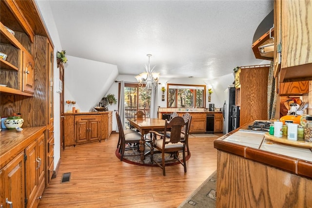 dining space with vaulted ceiling, light wood-type flooring, a textured ceiling, and a chandelier