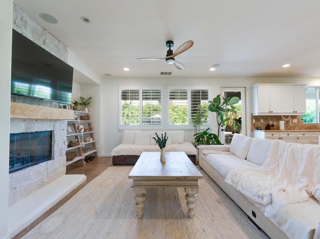 living room with ceiling fan, a healthy amount of sunlight, and a stone fireplace