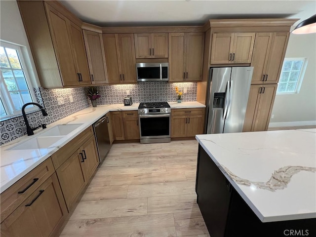 kitchen featuring sink, decorative backsplash, light hardwood / wood-style floors, light stone counters, and stainless steel appliances