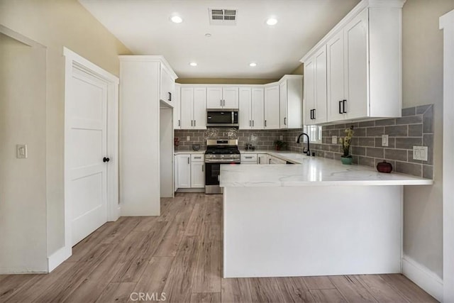 kitchen featuring backsplash, sink, light hardwood / wood-style floors, white cabinetry, and stainless steel appliances