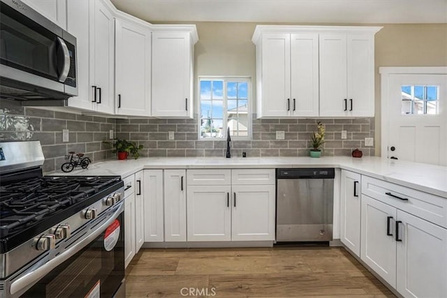 kitchen with appliances with stainless steel finishes, light wood-type flooring, white cabinetry, and sink