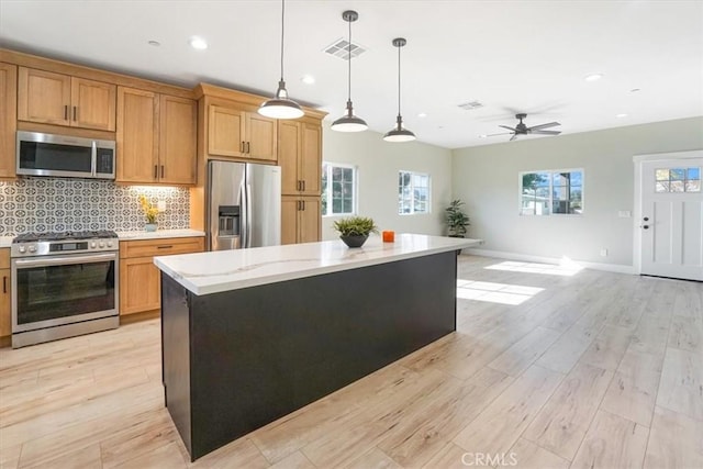 kitchen featuring decorative light fixtures, a center island, stainless steel appliances, and light hardwood / wood-style flooring