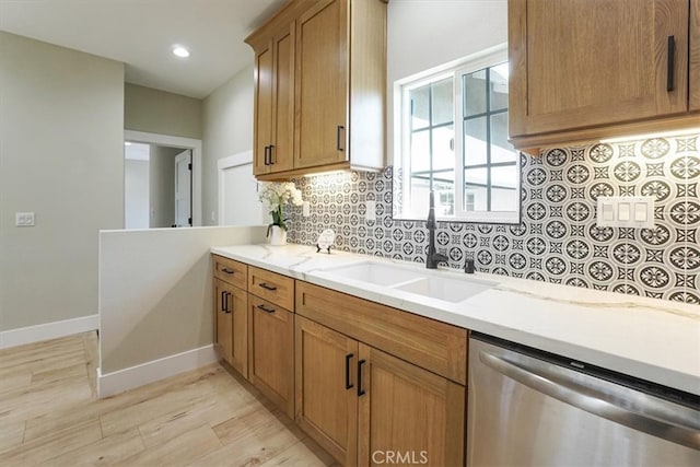 kitchen with backsplash, sink, stainless steel dishwasher, light stone countertops, and light wood-type flooring