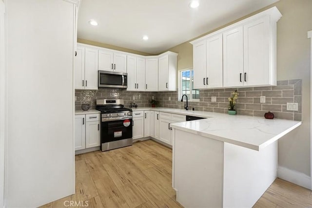 kitchen with white cabinetry, light hardwood / wood-style flooring, kitchen peninsula, decorative backsplash, and appliances with stainless steel finishes