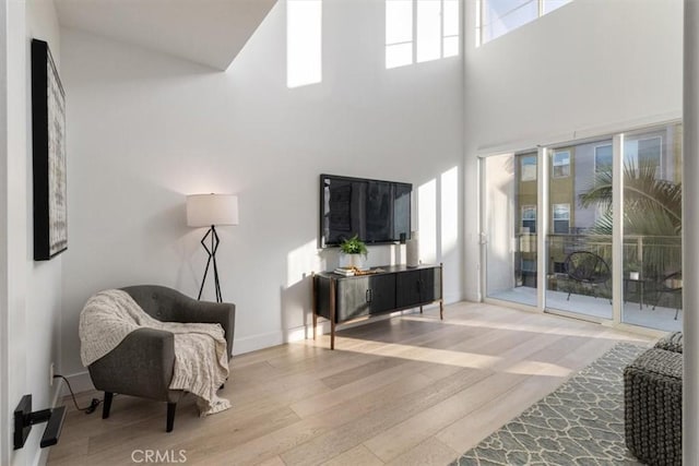 living area with light wood-style floors, a towering ceiling, and baseboards