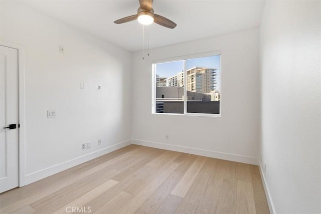 unfurnished room featuring a ceiling fan, a view of city, light wood-style flooring, and baseboards