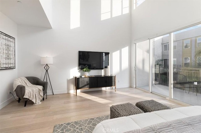 living room featuring baseboards, a towering ceiling, and light wood-style floors