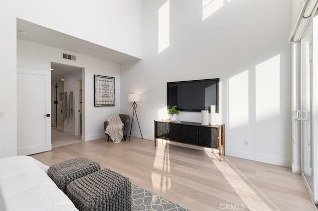 bedroom with a towering ceiling, wood finished floors, visible vents, and baseboards