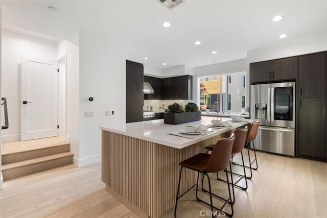 kitchen featuring a kitchen island, a kitchen breakfast bar, light countertops, refrigerator with glass door, and exhaust hood