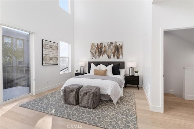 bedroom with access to outside, baseboards, light wood-style flooring, and a towering ceiling