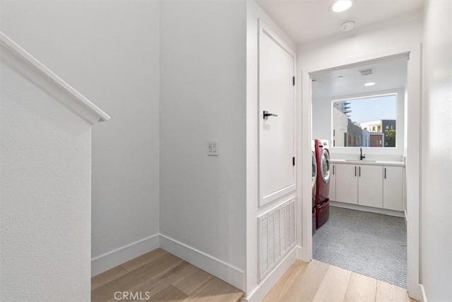 hall featuring light wood finished floors, baseboards, visible vents, washer and clothes dryer, and a sink