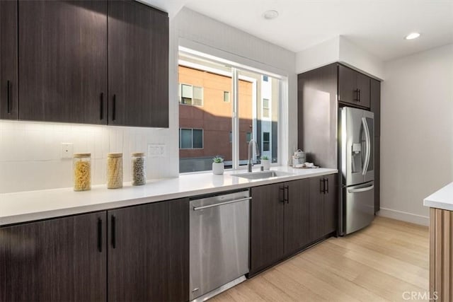 kitchen with stainless steel appliances, dark brown cabinets, light countertops, light wood-type flooring, and a sink