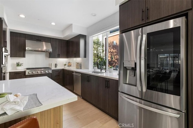 kitchen featuring appliances with stainless steel finishes, light countertops, light wood-type flooring, under cabinet range hood, and a sink