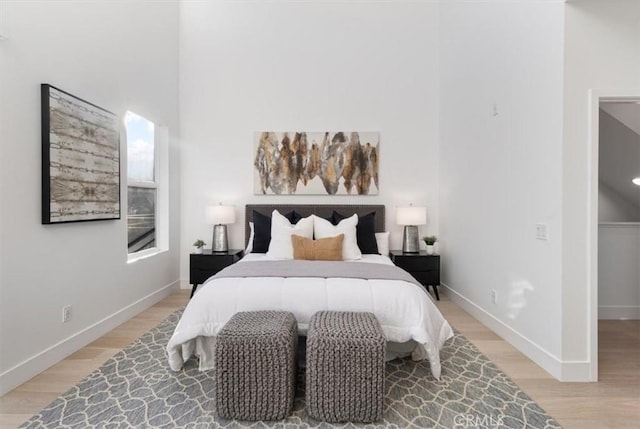 bedroom with light wood finished floors, a towering ceiling, and baseboards