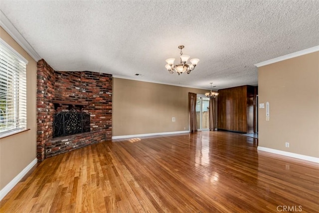 unfurnished living room with a textured ceiling, crown molding, a notable chandelier, a fireplace, and hardwood / wood-style floors