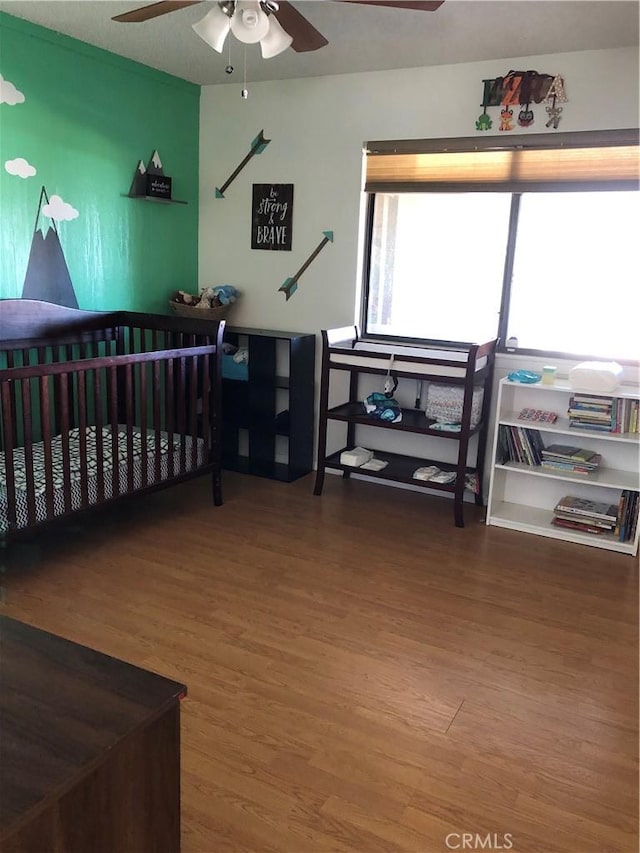 bedroom featuring a nursery area, hardwood / wood-style flooring, and ceiling fan